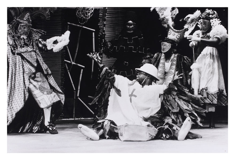 Photograph of actors on stage, one seated on the ground from Maskarade