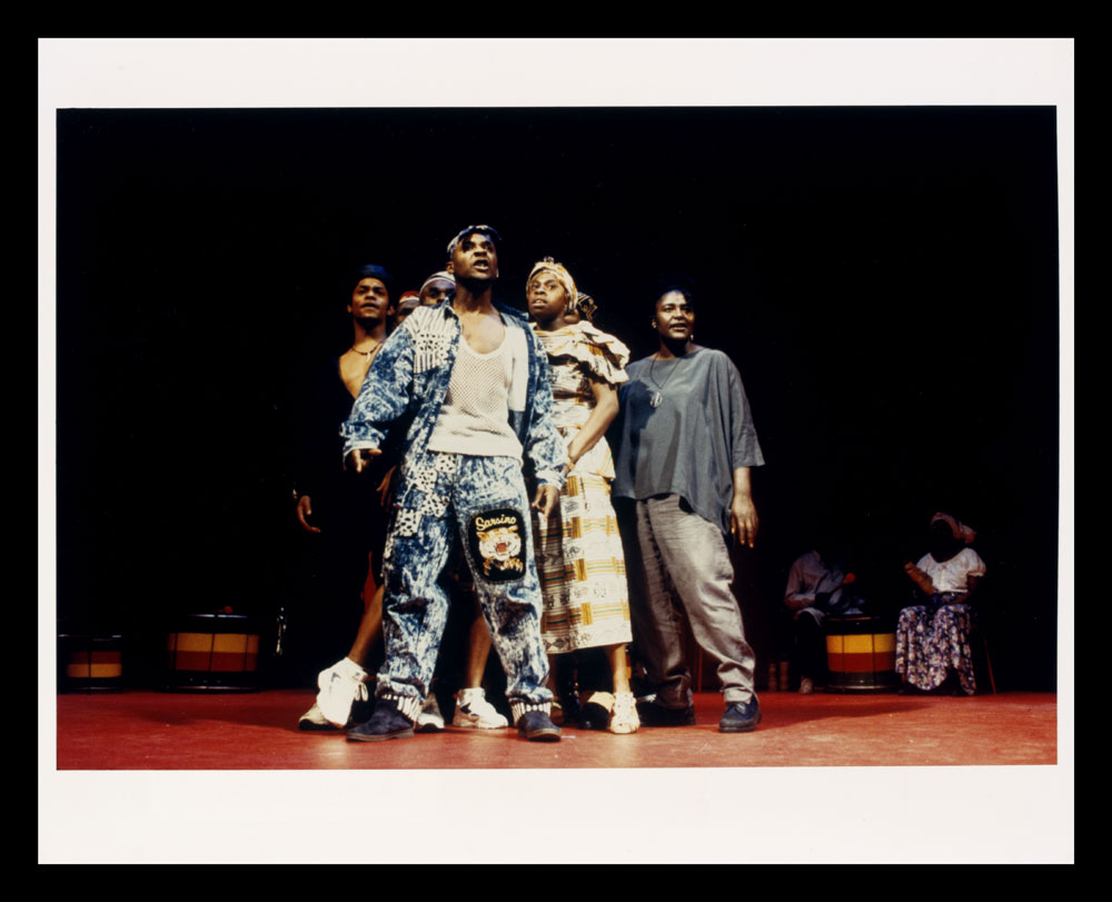 Colour photo of actors on stage, man in denim in front, from Zumbi